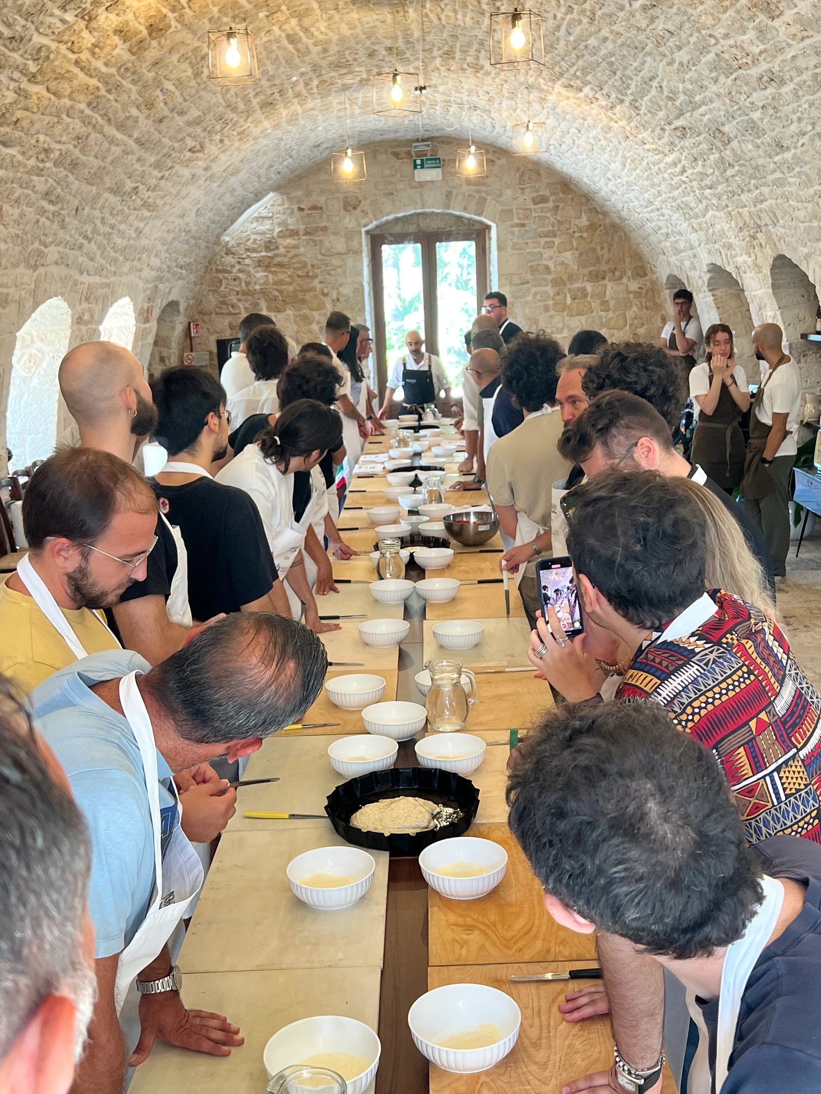 Team building in cucina: i partecipanti al lavoro lungo una tavolata sotto una volta in pietra