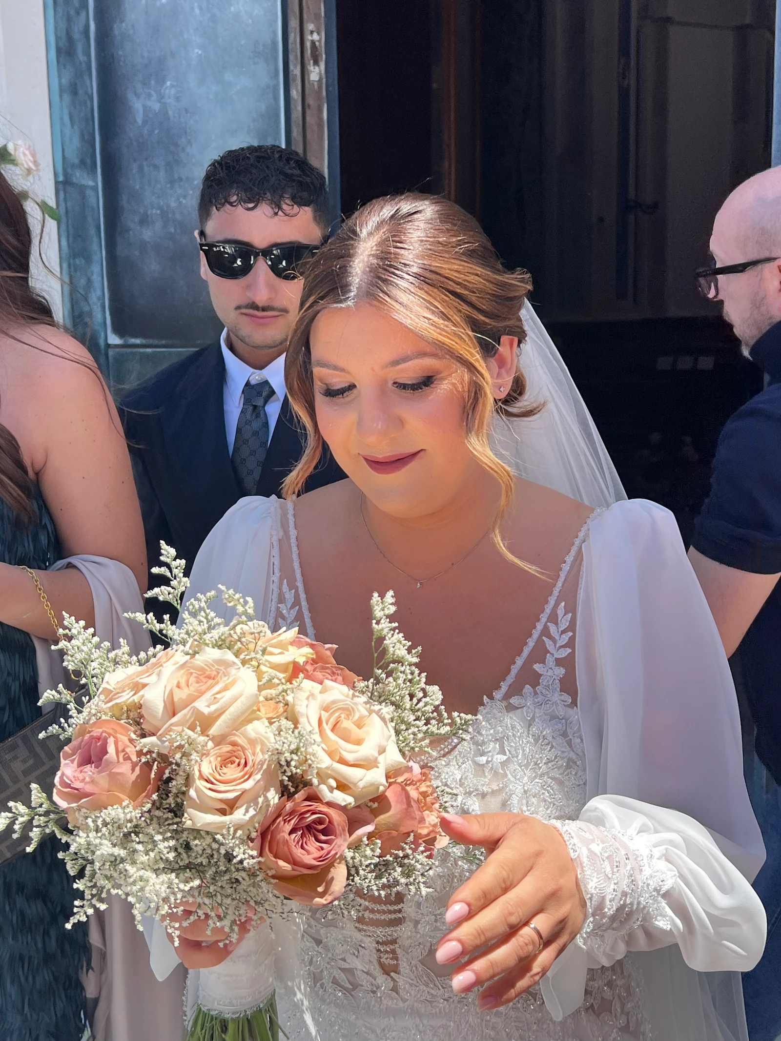 La sposa guarda il bouquet di rose cipria all’uscita della chiesa