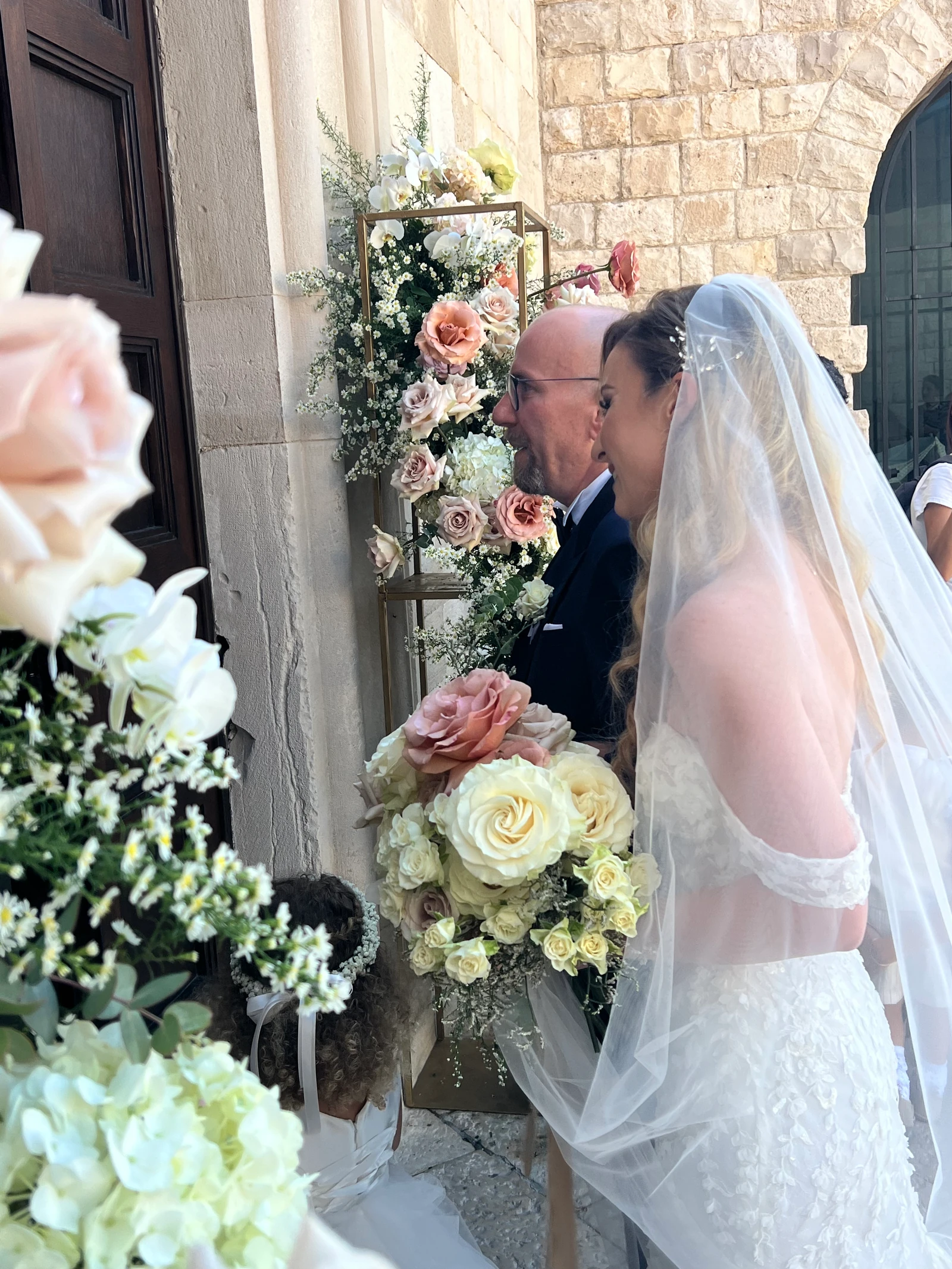 La sposa accompagnata all’ingresso della chiesa, tra rose e fiori bianchi