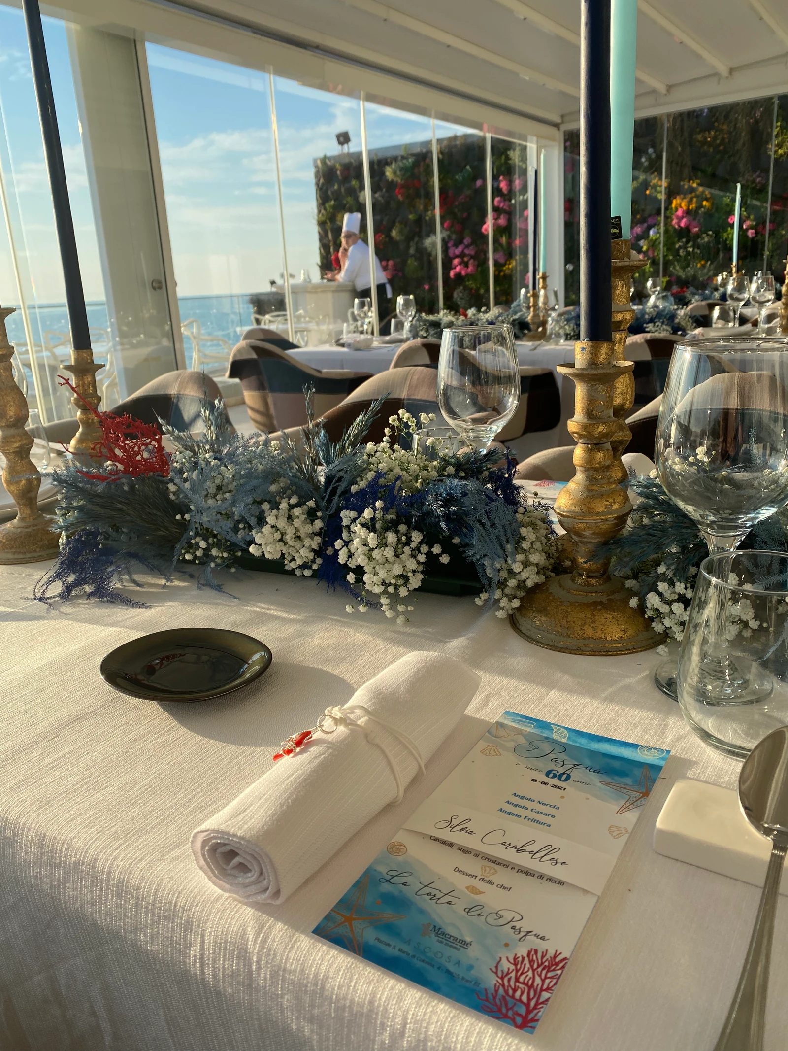Tavola con candelieri dorati e fiori blu in una sala vista mare